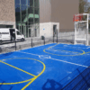 Deze mini multi sportkooi is uitgevoerd met een blauwe rolcoating > Granuplast met witte voetbal belijning en gele basketbalbelijning. Locatie Amsterdam.