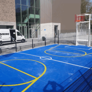 Deze mini multi sportkooi is uitgevoerd met een blauwe rolcoating > Granuplast met witte voetbal belijning en gele basketbalbelijning. Locatie Amsterdam.