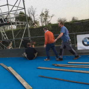 Op de afbeelding de vrijwilligers van Hockey in Hoegaarden bezig met de vervanging van de oude houten slagplanken door onze regenraat slagplanken.