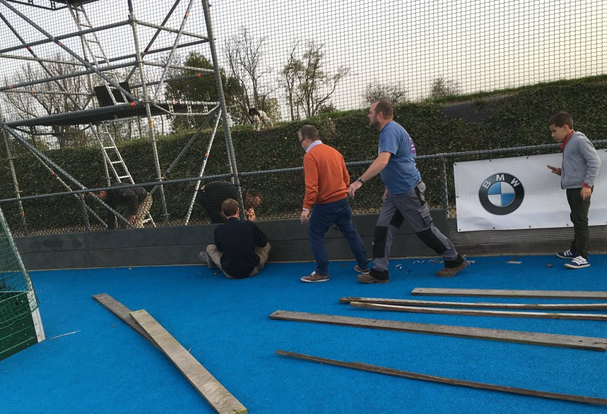 Op de afbeelding de vrijwilligers van Hockey in Hoegaarden bezig met de vervanging van de oude houten slagplanken door onze regenraat slagplanken.
